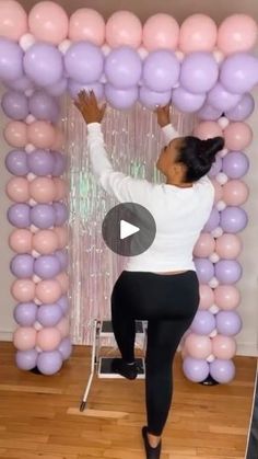 a woman standing in front of a giant balloon arch with balloons on the wall behind her