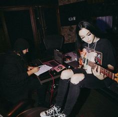 two people sitting in a room with guitars and recording equipment on the floor, one person holding a guitar