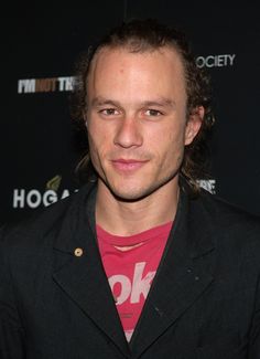 a man with long hair wearing a red shirt and black blazer posing for the camera