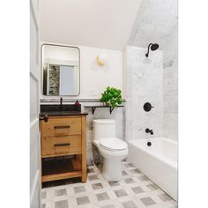 a white toilet sitting next to a bath tub under a bathroom mirror on top of a wooden cabinet