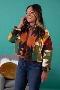 a woman standing in front of a couch talking on a cell phone and smiling at the camera