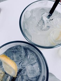 two glasses filled with ice and one has a banana peel on the rim, while another holds a spoon in it