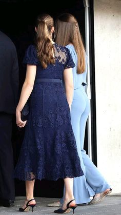 two women in blue dresses are walking out of a building with their hands behind them