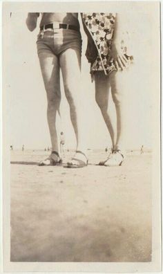 an old black and white photo of two people standing next to each other on the beach