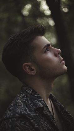 a man standing in the woods looking up at something with his head tilted to the side