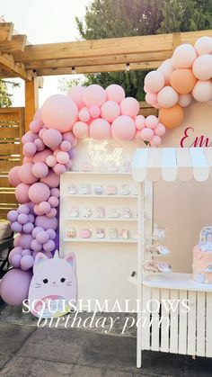 a dessert stand with pink and purple balloons on the wall, an animal cake table and a cat figurine next to it