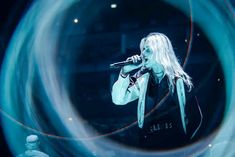 a woman with long white hair holding a microphone in front of a circular object on stage