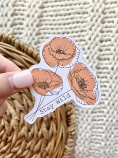 a person holding up a sticker with flowers on it in front of a basket