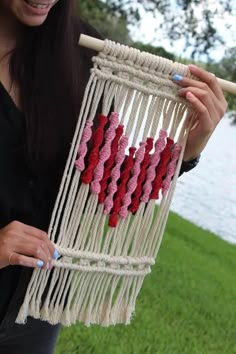 a woman holding up a macrame with hearts on it in front of water