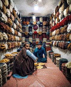 two men sitting on the floor in a room full of hats and rugs,