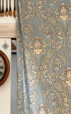 a clock is hanging on the wall next to a blue and gold floral print curtain