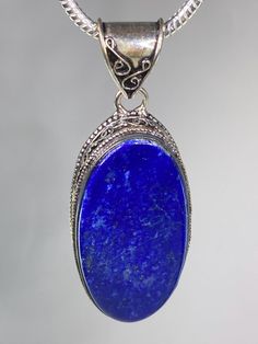 A majestic deep Blue Lapis Lazuli and silver pendant including the sterling silver 18 inch snake chain. The stone is of a good size, a vivid royal blue Lapis Lazuli stone, oval-cut and set in a classic half-bezel. The setting is of a contemporary design and adds a little flair to this piece. The pendant measures 4.6cm long x 2.5cm wide and 0.9cm deep. Pendant weight - 21 grams. This pendant is sold including the classic 3mm diameter sterling silver snake chain. This chain is 45cm or 18in long. A Blue Lapis Lazuli Oval Jewelry, Oval Lapis Lazuli Silver Jewelry, Oval Silver Lapis Lazuli Jewelry, Silver Jewelry With Oval Lapis Lazuli, Blue Stamped 925 Oval Pendant Jewelry, Blue Oval Pendant Jewelry, Engraved, Blue Engraved Oval Pendant Jewelry, Half Bezel, Lapis Lazuli Stone