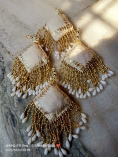 three pairs of gold and white beaded chandelier earrings on the ground with sunlight shining through them