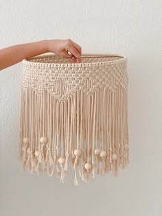 a hand holding a macrame lamp shade with tassels and beads on it