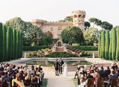 an outdoor wedding ceremony in front of a castle with lots of greenery and trees