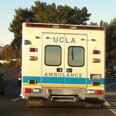 an ambulance is driving down the road with trees in the backgrouund and cars behind it