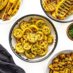 three plates filled with grilled vegetables on top of a white tablecloth next to bowls of pesto