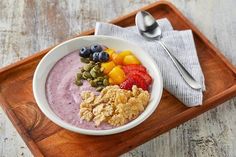 a bowl of oatmeal with fruit and granola on a wooden tray