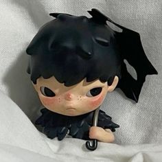 a little doll with black hair and an umbrella in its mouth sitting on a white sheet