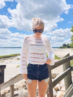 a woman standing on a wooden bridge next to the ocean with her hands in her pockets