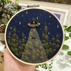 someone is holding up a embroidery project with trees and an alien spaceship in the sky