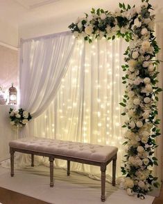 a wedding ceremony setup with white flowers and greenery on the wall, along with a bench