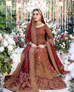 a woman in a red and gold bridal gown sitting on a floral decorated stage