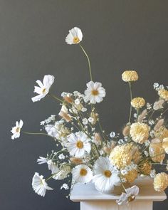 a white vase filled with lots of flowers on top of a wooden table next to a gray wall