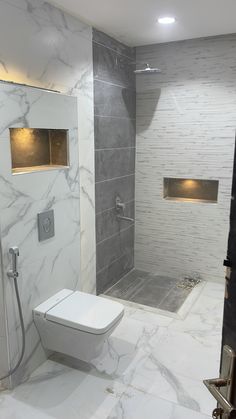 a white toilet sitting inside of a bathroom next to a walk in shower and tiled walls