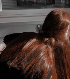 a woman with long red hair sitting in front of a window looking out the window