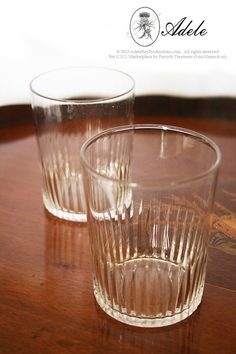 two clear glass cups sitting on top of a wooden table next to another glass cup