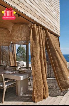 an outdoor dining area on the deck overlooking the ocean with curtains hanging from it's roof