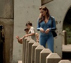 a woman in blue jumpsuit standing next to a man on the stairs with other people behind her