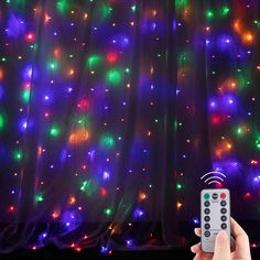 a person holding a remote control in front of a curtain covered with multicolored lights