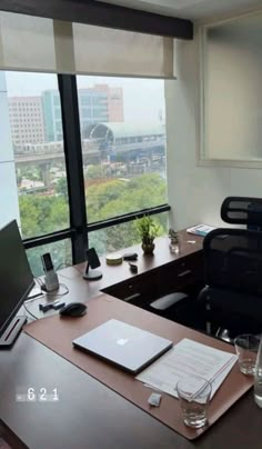 an office desk with a laptop computer on top of it next to a large window