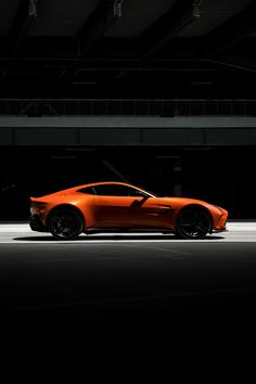 an orange sports car parked in a parking garage with dark lighting on the side of it