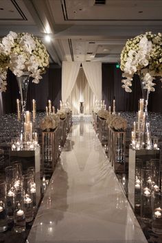 the aisle is lined with clear vases filled with flowers and candles