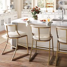 a kitchen with white cabinets and gold trimmings on the countertops, along with two bar stools