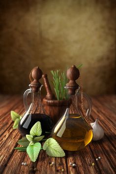 two bottles filled with different types of oils on top of a wooden table next to green leaves