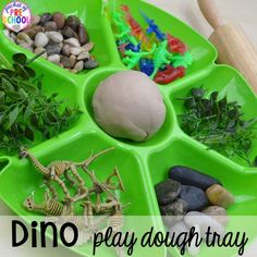 a green tray filled with rocks and plants next to a wooden rolling board that says dino play dough tray