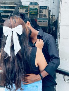 a man and woman embracing each other in front of a building with large white bows on their hair