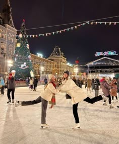 two people skating on an ice rink in front of a lit up christmas tree at night