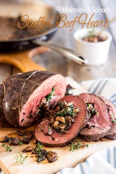 a close up of sliced meat on a cutting board with mushrooms and herbs next to it