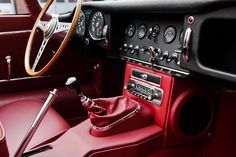 the interior of an old fashioned car with red leather and wood trims, including steering wheel