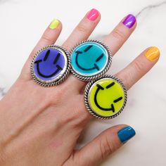 three rings with smiley faces on them sitting on top of a marble countertop in front of a woman's hand