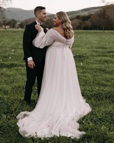 a man and woman in formal wear standing together on the grass with their arms around each other