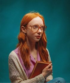 a woman with red hair and glasses holding a book