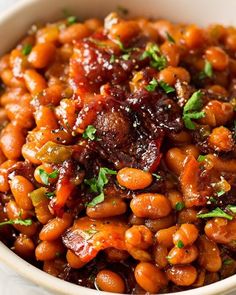 a white bowl filled with baked beans and garnished with parsley on top