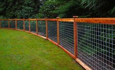 a wooden and wire fence is shown in front of some green grass with trees behind it