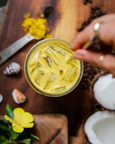 a person is holding a glass with yellow liquid in it and some flowers on the table